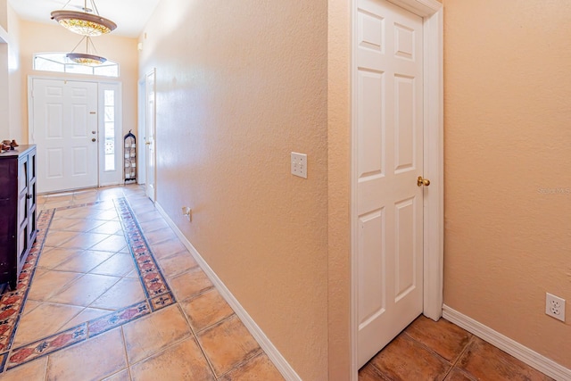 foyer featuring a textured wall, baseboards, and light tile patterned floors