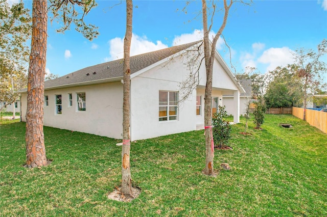 rear view of property with stucco siding, fence, and a yard