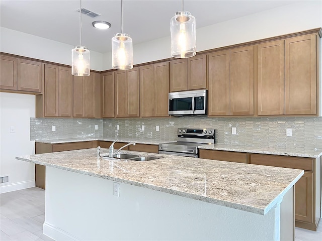 kitchen with an island with sink, light stone counters, stainless steel appliances, visible vents, and a sink