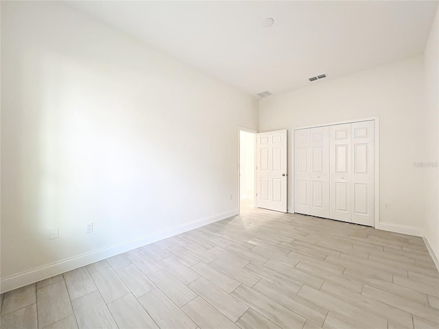 unfurnished bedroom featuring light wood-type flooring, baseboards, visible vents, and a closet