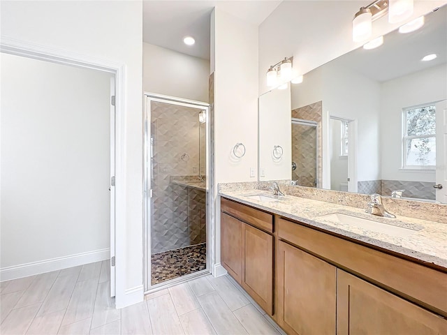 full bathroom with baseboards, double vanity, a stall shower, and a sink