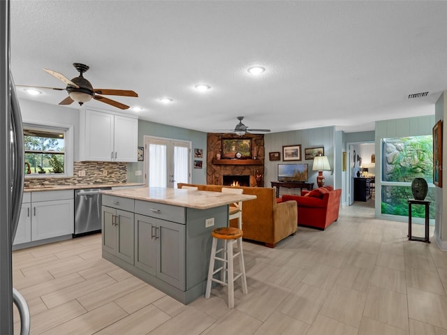 1139 Fairway Dr, Winter Park, FL 32792 - kitchen featuring a ceiling fan, stainless steel appliances, a fireplace, white cabinets, and a breakfast bar area