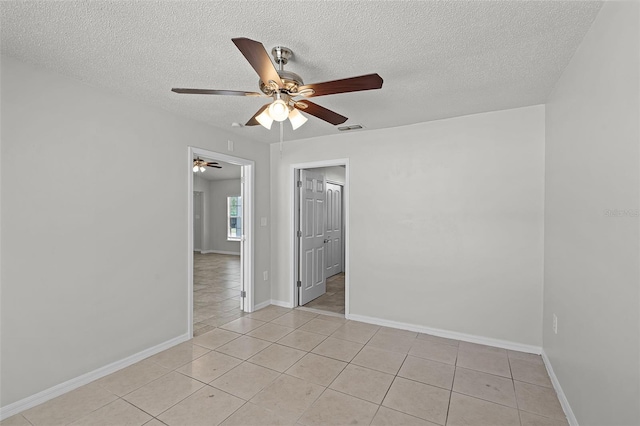 spare room featuring visible vents, a ceiling fan, light tile patterned floors, baseboards, and a textured ceiling
