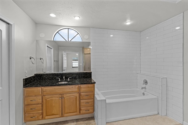 full bath with tile patterned flooring, a tub to relax in, vanity, and a textured ceiling