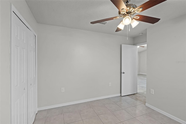 unfurnished bedroom with a ceiling fan, a textured ceiling, a closet, light tile patterned flooring, and baseboards