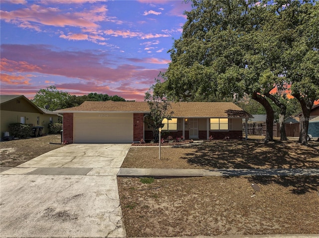 ranch-style house with fence, a shingled roof, concrete driveway, an attached garage, and brick siding
