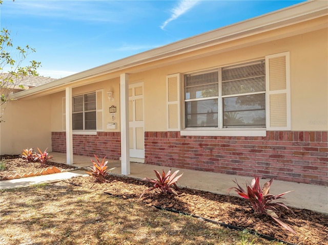 property entrance featuring brick siding, a porch, and stucco siding
