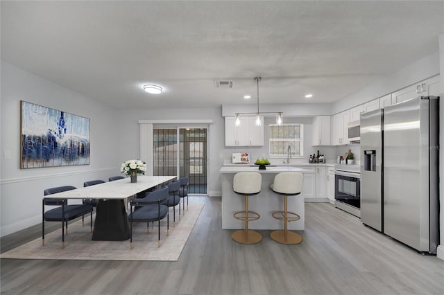 kitchen featuring stainless steel fridge with ice dispenser, visible vents, light wood-style floors, baseboards, and range