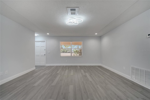 empty room with a textured ceiling, wood finished floors, visible vents, and baseboards