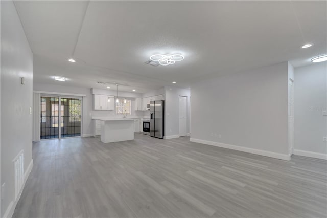 unfurnished living room with a sink, light wood-style floors, baseboards, visible vents, and recessed lighting