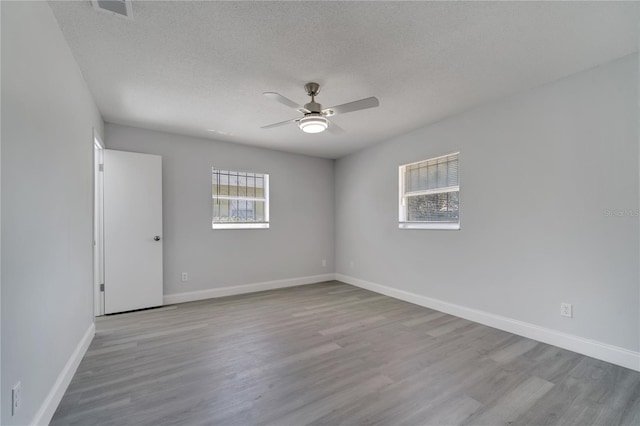 empty room with baseboards, a ceiling fan, wood finished floors, and a textured ceiling