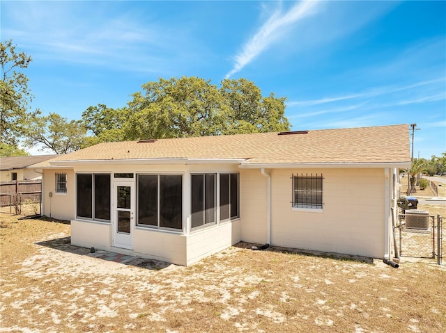 back of house with concrete block siding, roof with shingles, a sunroom, and fence