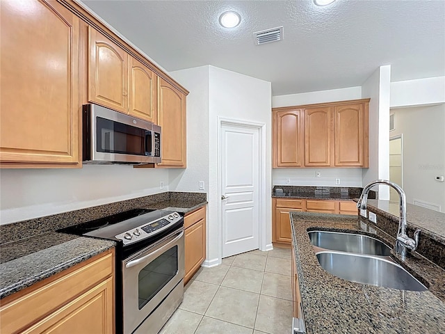 kitchen with stainless steel appliances, a textured ceiling, a sink, dark stone countertops, and light tile patterned floors
