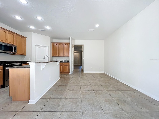 kitchen featuring stainless steel microwave, a center island with sink, recessed lighting, range, and light tile patterned floors