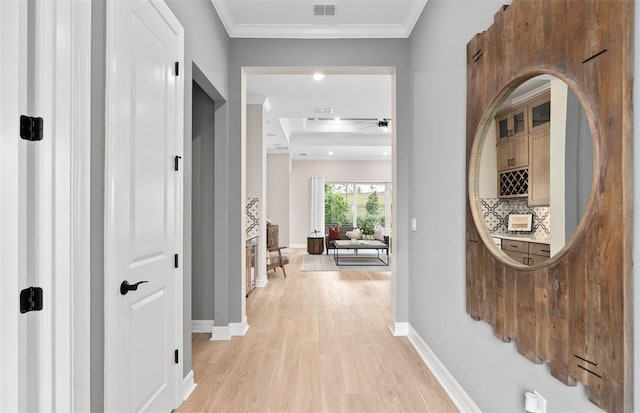 hallway with light wood-type flooring, baseboards, visible vents, and ornamental molding