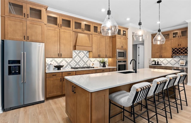 kitchen with stainless steel appliances, a sink, light wood-type flooring, decorative backsplash, and premium range hood