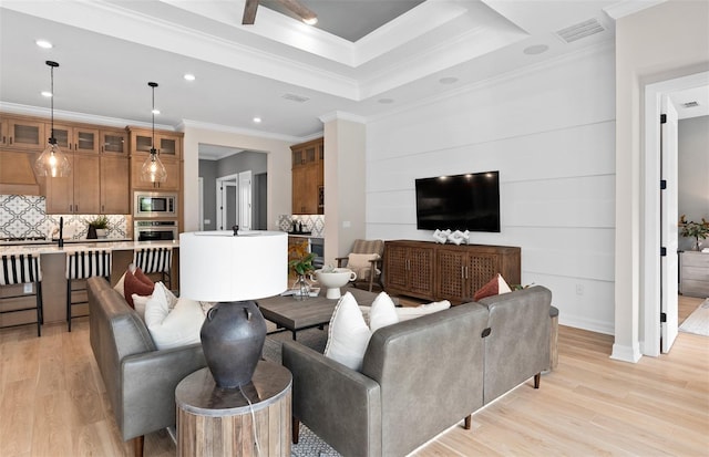 living room with light wood finished floors, a tray ceiling, visible vents, recessed lighting, and crown molding