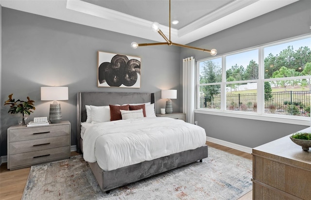 bedroom featuring baseboards, ornamental molding, a tray ceiling, and wood finished floors