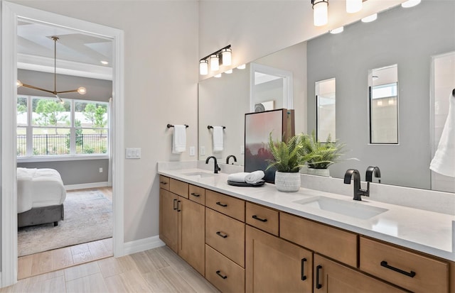 ensuite bathroom featuring baseboards, a sink, double vanity, and an inviting chandelier