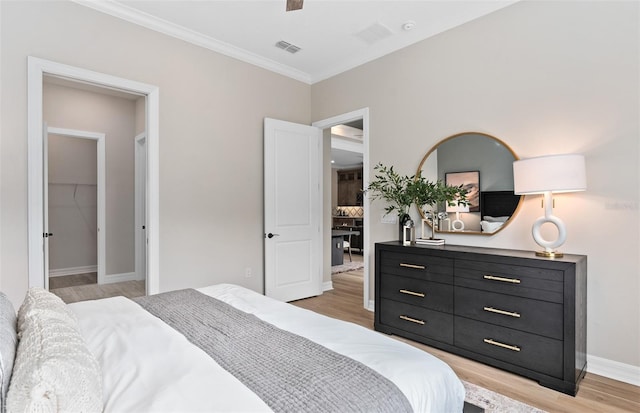 bedroom featuring a walk in closet, light wood-style flooring, baseboards, ornamental molding, and visible vents