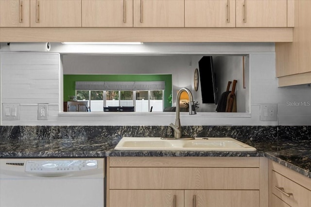 kitchen with dishwasher, light brown cabinetry, a sink, and dark stone countertops