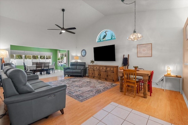 living area featuring baseboards, light wood-style flooring, a ceiling fan, and high vaulted ceiling