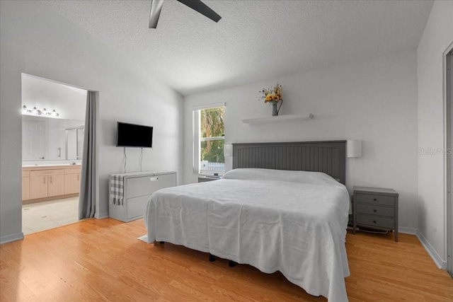 bedroom with connected bathroom, lofted ceiling, a textured ceiling, and light wood-style flooring