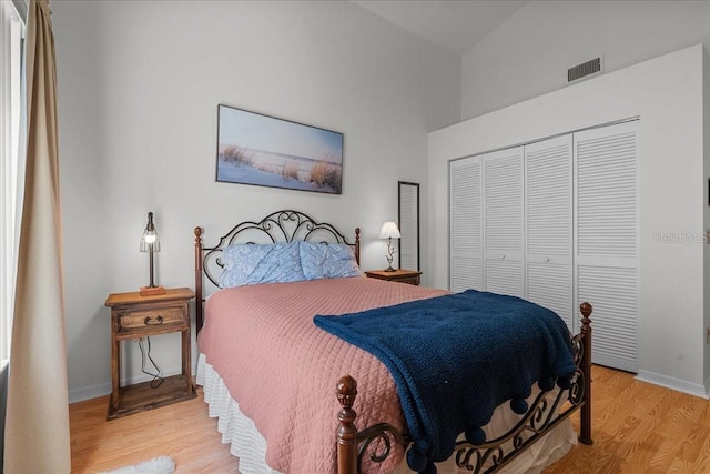 bedroom with baseboards, wood finished floors, visible vents, and a closet