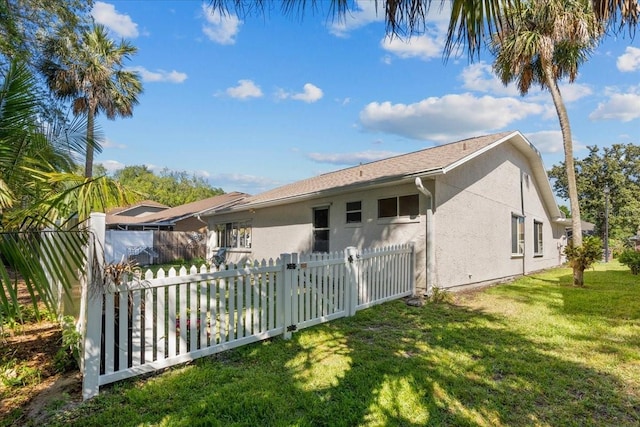 rear view of property featuring fence, a lawn, and stucco siding