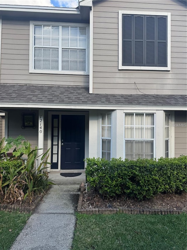 view of exterior entry with roof with shingles