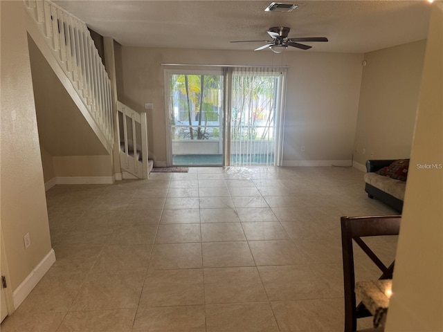 unfurnished living room with baseboards, a ceiling fan, visible vents, and stairway
