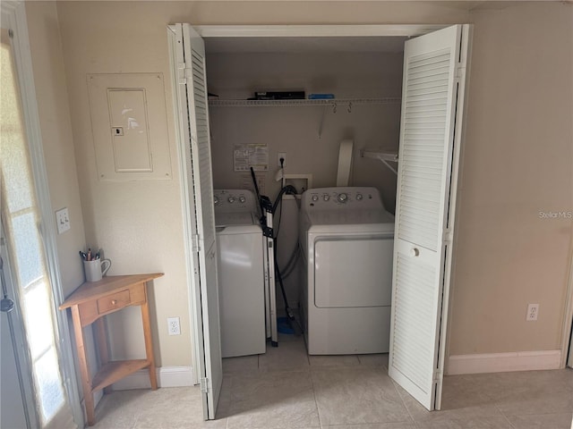 clothes washing area featuring laundry area, light tile patterned floors, electric panel, washing machine and clothes dryer, and baseboards