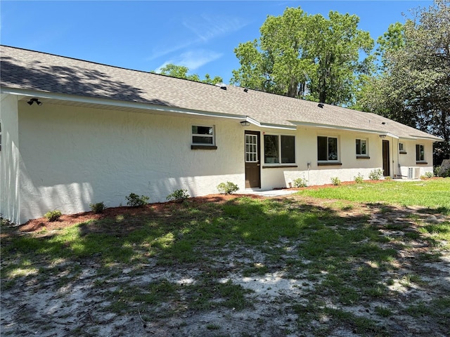 rear view of property with roof with shingles, a yard, and stucco siding