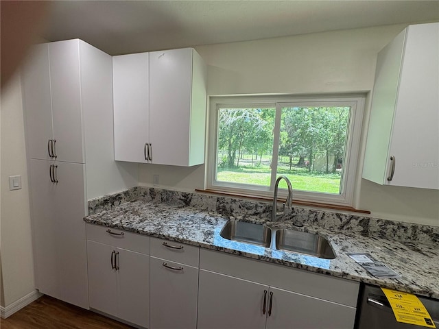 kitchen featuring a wealth of natural light, light stone counters, black dishwasher, and a sink