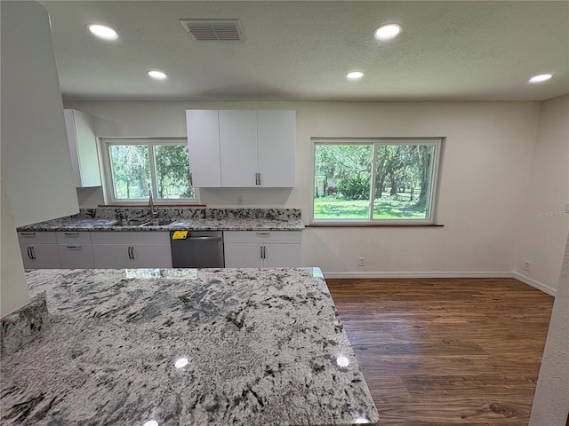 kitchen featuring light stone counters, dishwasher, visible vents, a healthy amount of sunlight, and a sink