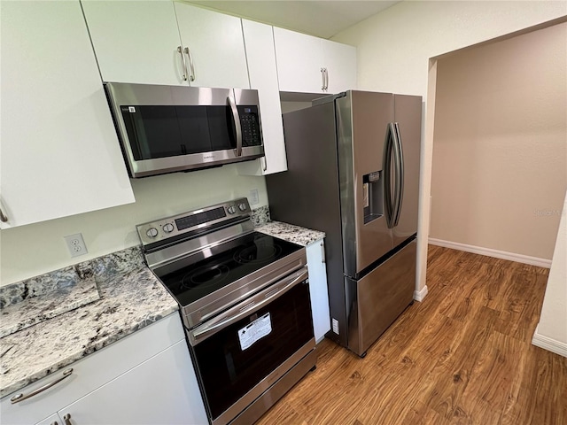 kitchen with stainless steel appliances, wood finished floors, light stone countertops, baseboards, and white cabinetry