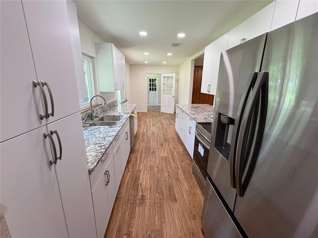 kitchen with white cabinets, wood finished floors, a sink, light stone countertops, and appliances with stainless steel finishes