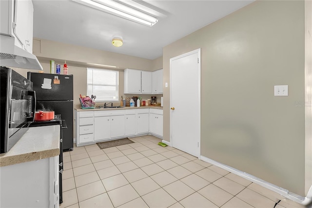 kitchen with a sink, white cabinetry, light countertops, under cabinet range hood, and freestanding refrigerator