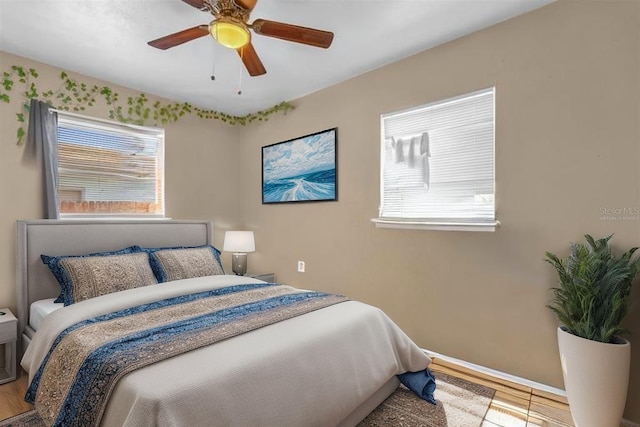 bedroom featuring baseboards, a ceiling fan, wood finished floors, and multiple windows