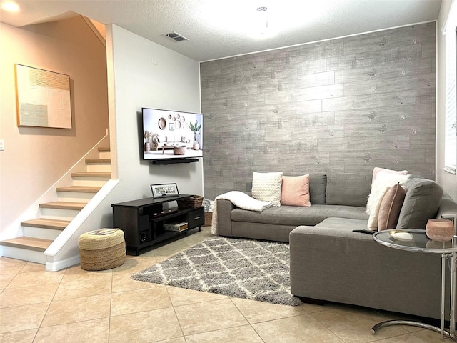 living room with an accent wall, stairway, visible vents, and tile patterned flooring