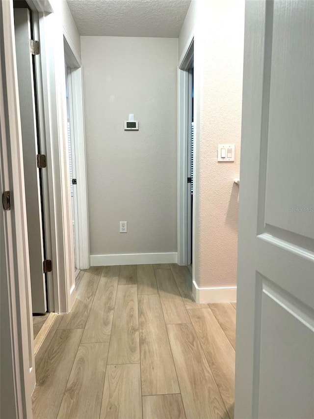 corridor with wood finished floors, a textured ceiling, and baseboards