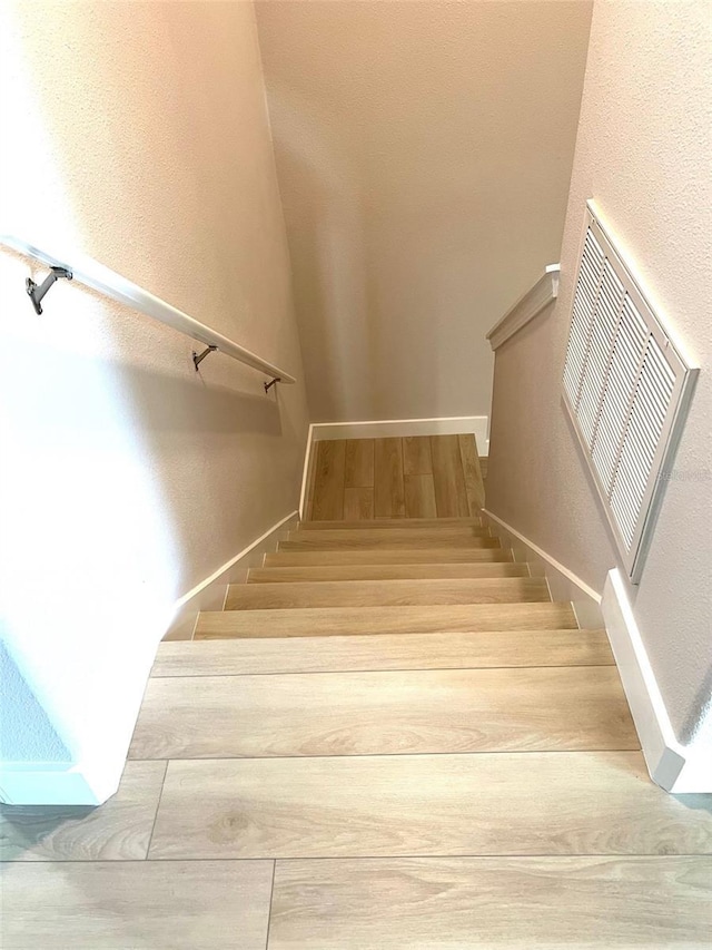 stairway with visible vents, a textured wall, and wood finished floors