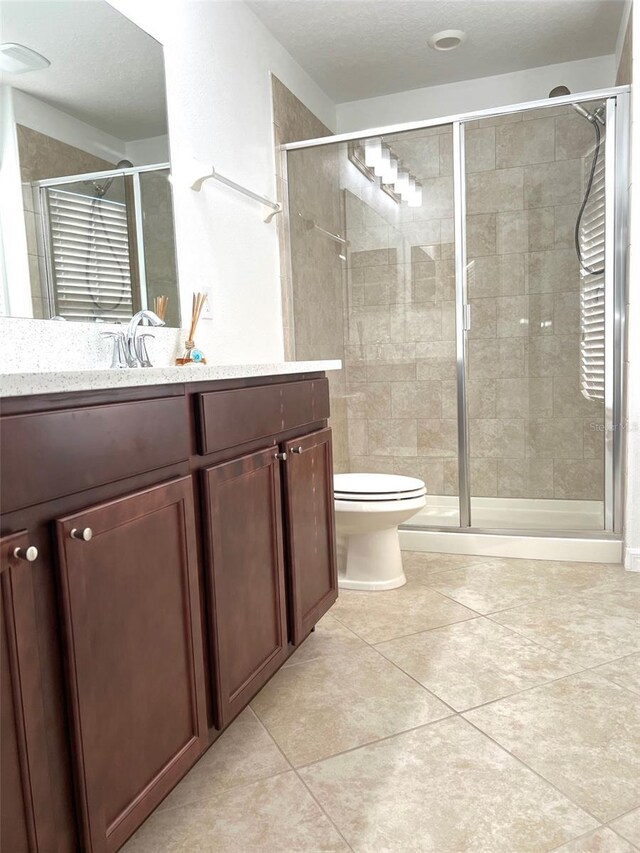 full bathroom featuring toilet, vanity, tile patterned flooring, and a stall shower
