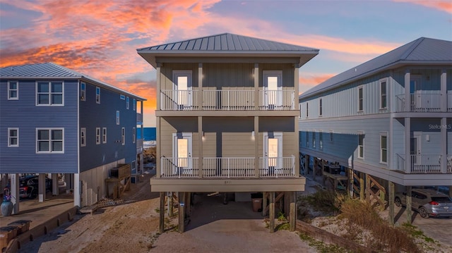 back of property at dusk with a carport, driveway, a balcony, and metal roof