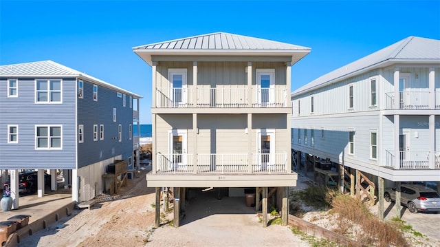 rear view of property featuring a carport, a balcony, dirt driveway, and metal roof