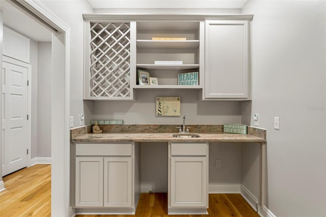 kitchen featuring open shelves, a sink, light wood-style floors, light stone countertops, and baseboards