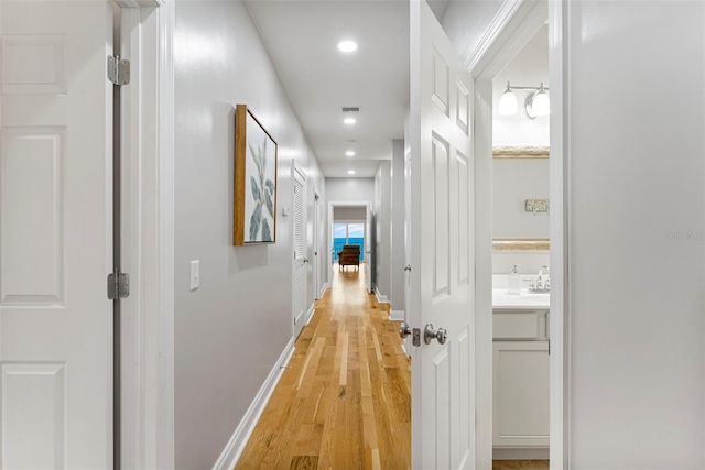 hallway featuring a sink, baseboards, visible vents, recessed lighting, and light wood-style floors