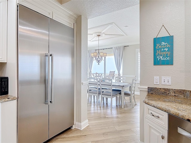 4071 S Atlantic Ave Unit 803, New Smyrna Beach, FL 32169 - kitchen featuring built in fridge, a chandelier, white cabinetry, light wood-type flooring, and a textured wall