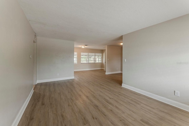 empty room featuring a textured ceiling, baseboards, and light wood-style floors