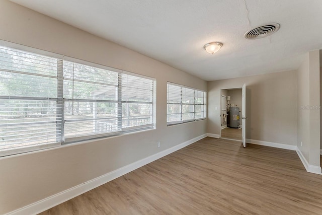 spare room with visible vents, light wood-style floors, baseboards, and electric water heater